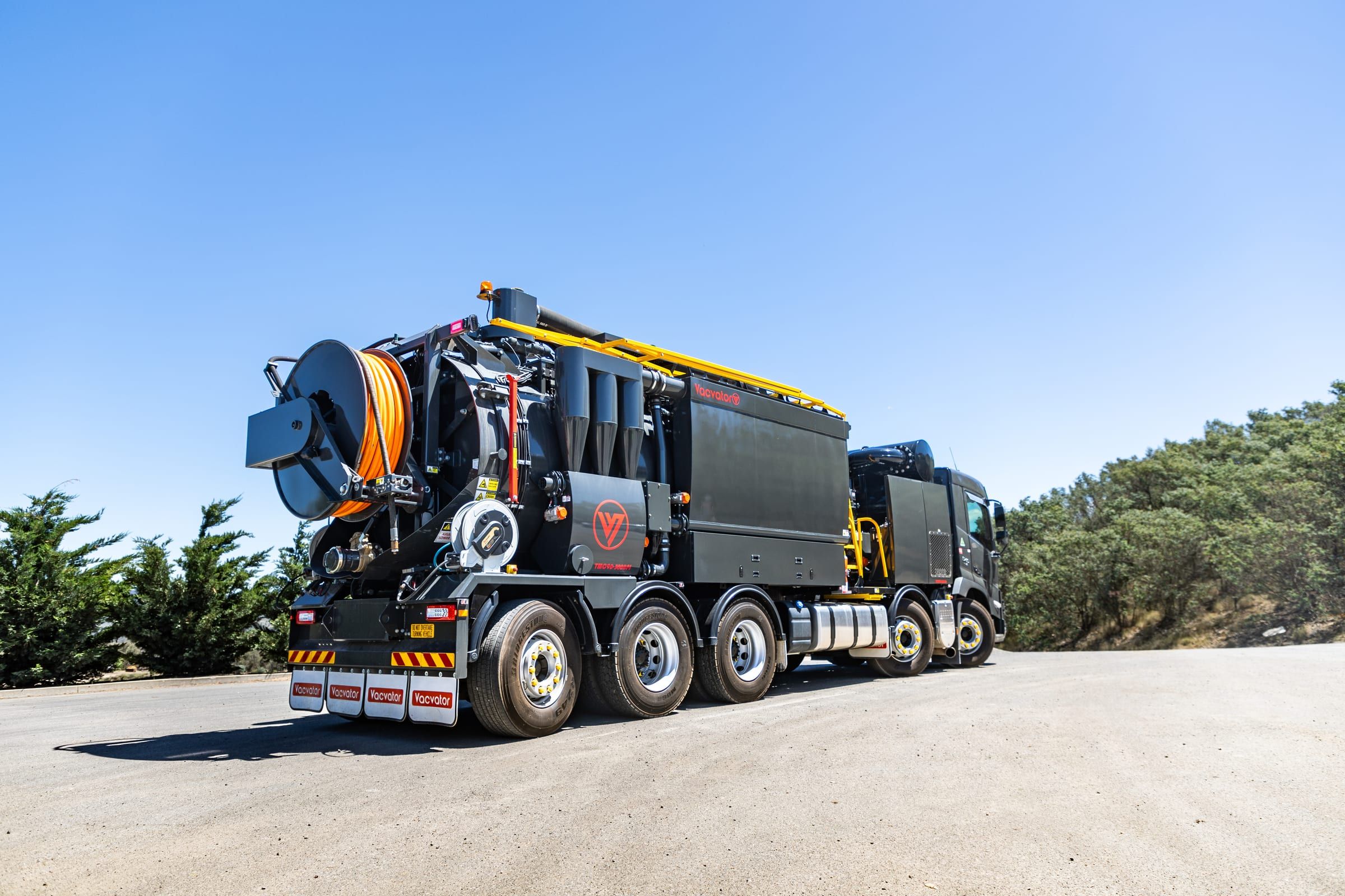 The HD 10-90 vacuum truck on a gravel yard under a clear blue sky, seen from the rear.