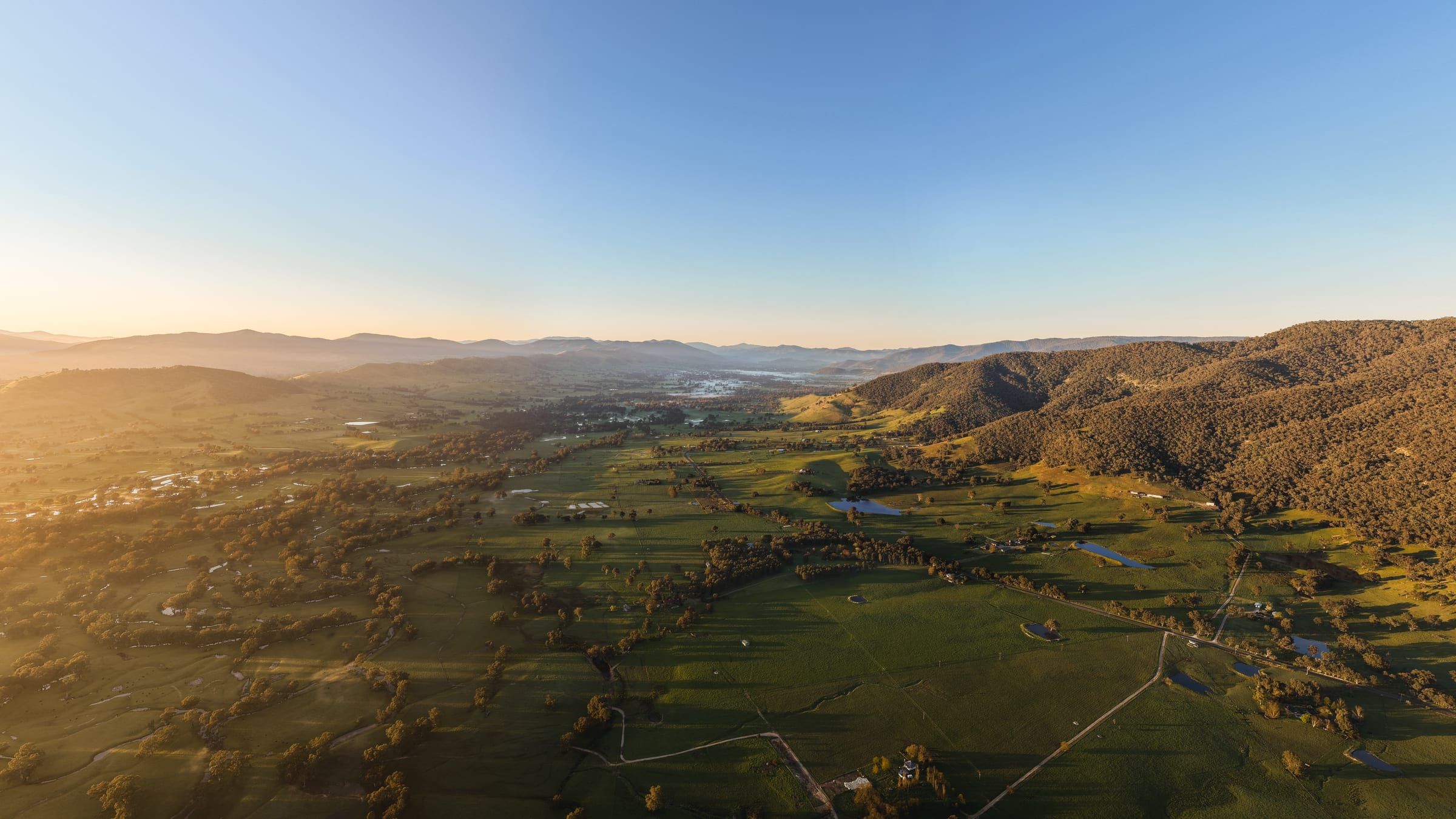 Looking along a valley of paddocks and farm tracks, with the hills catching the first light.