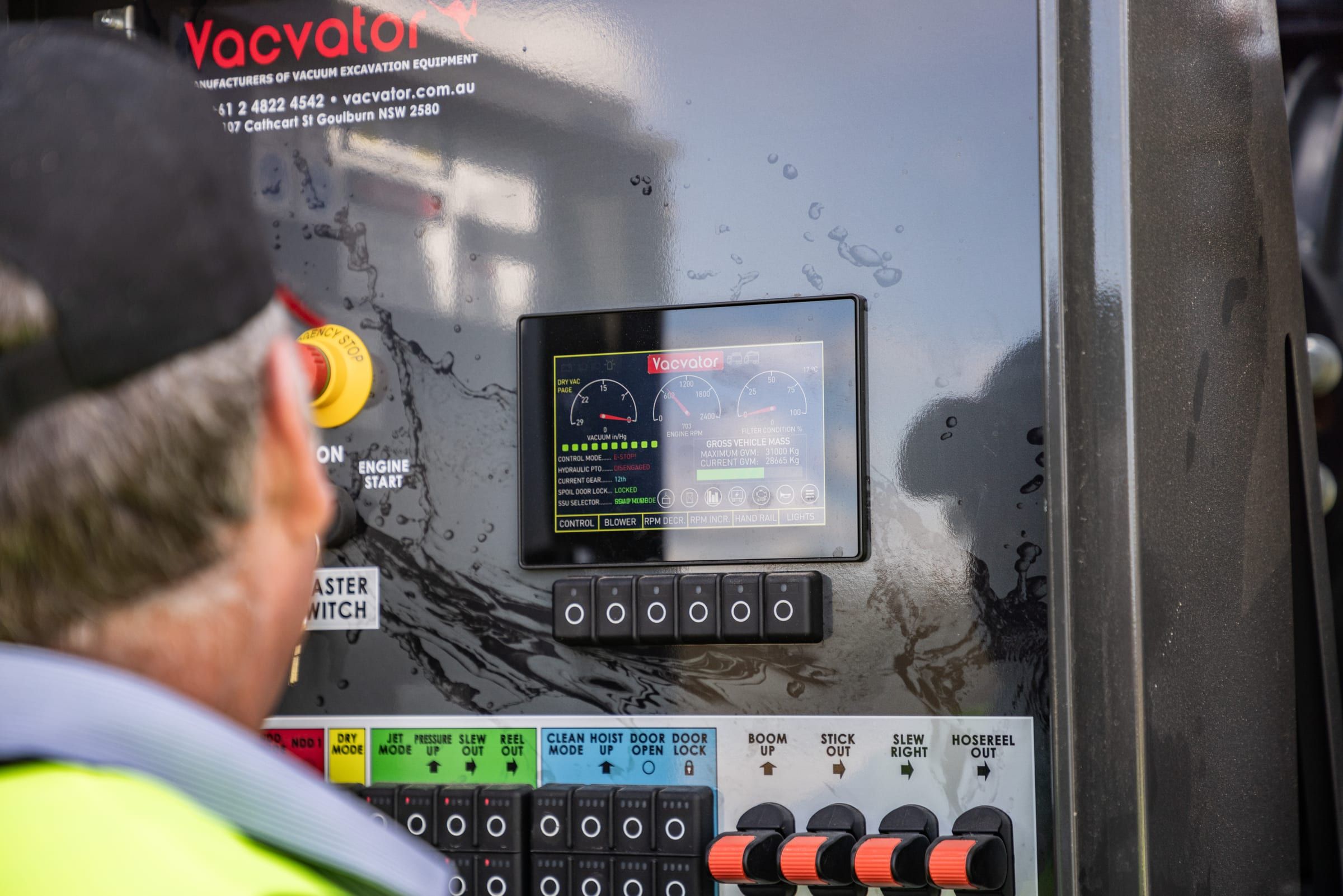 An operator checks the truck's control panel, with its screen and a row of labelled switches.