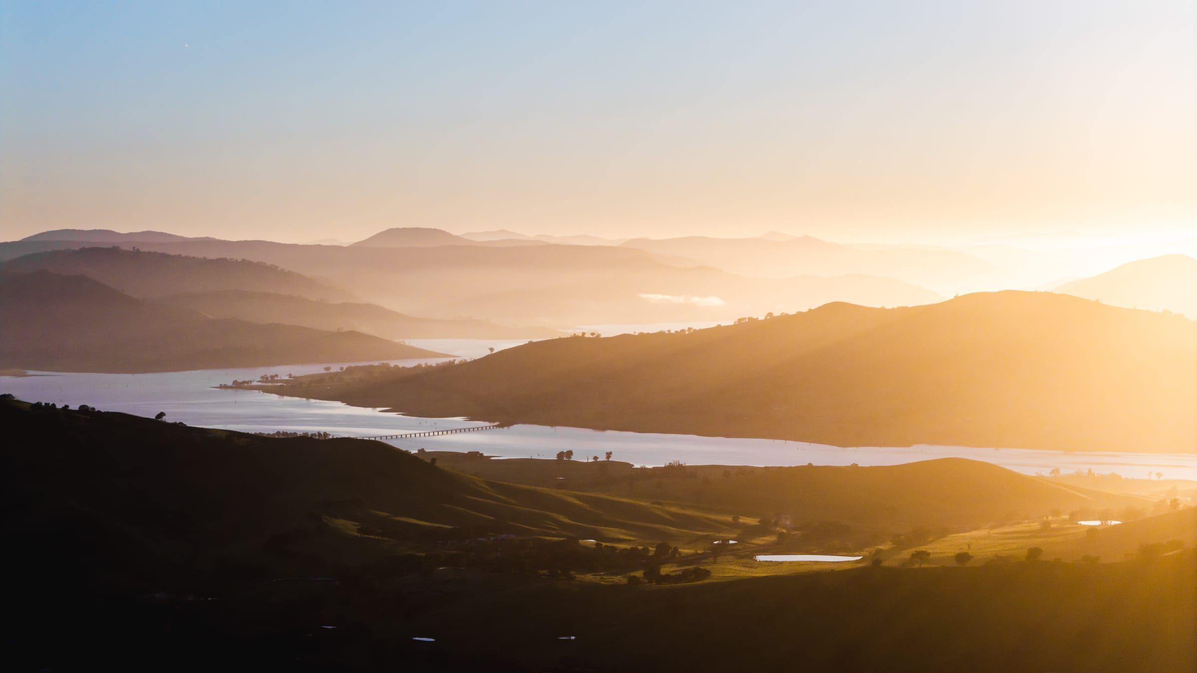 Layers of misty hills above a lake at sunrise, the water glowing orange.