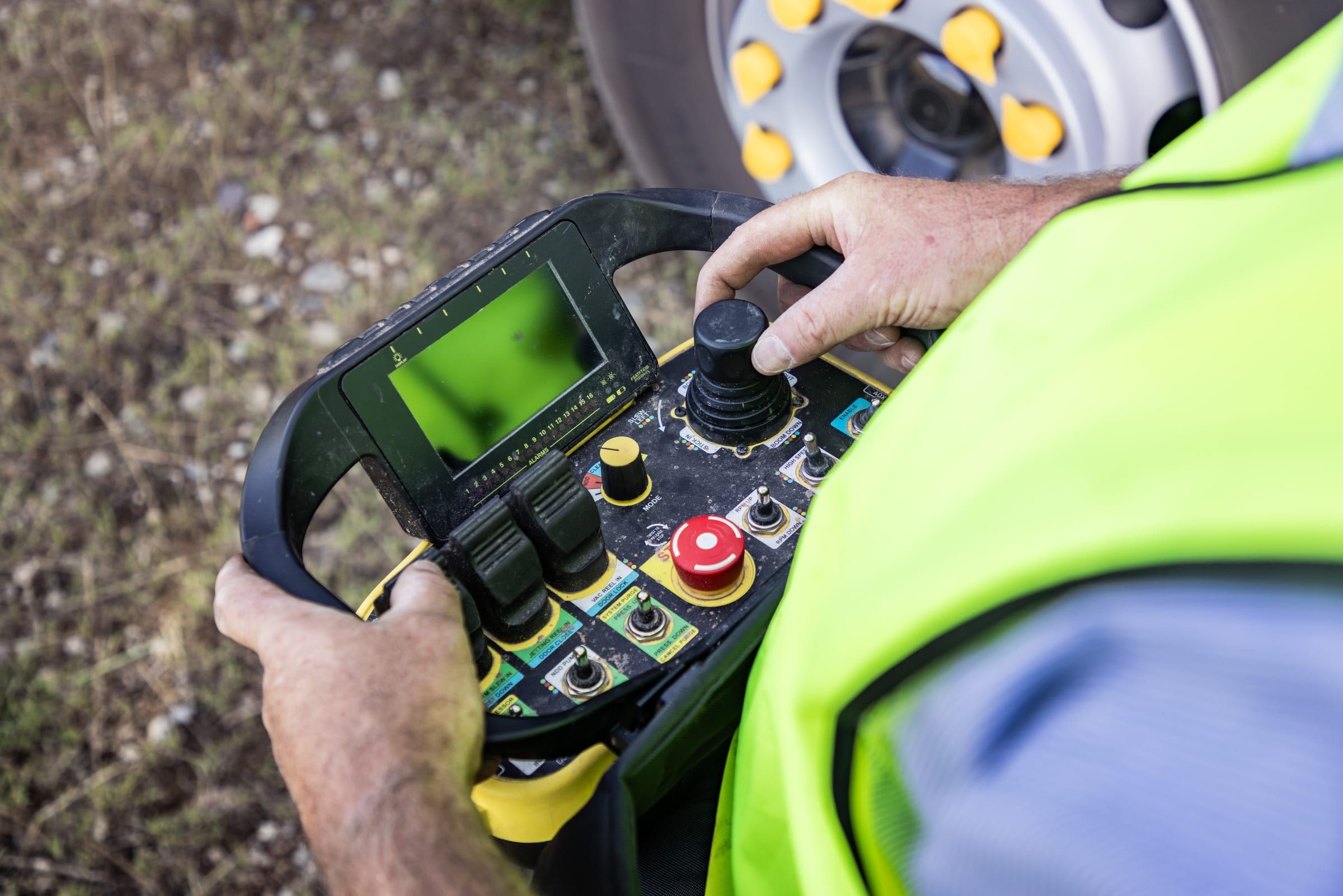 An operator's hands on the handheld remote, with a joystick and small screen.