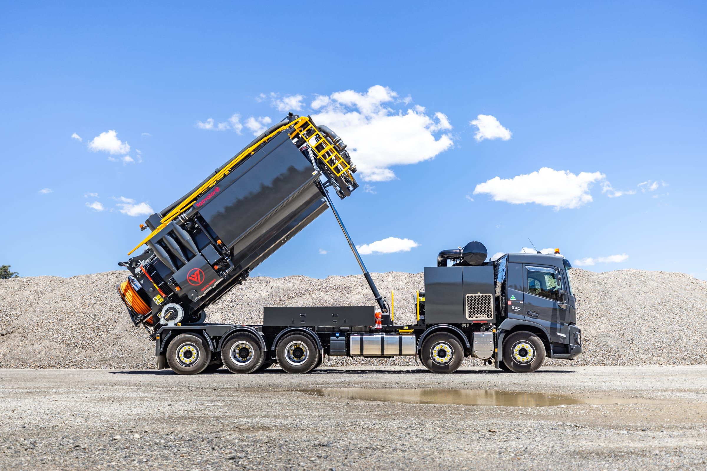 The truck tipping its tank to empty spoil onto a gravel yard.