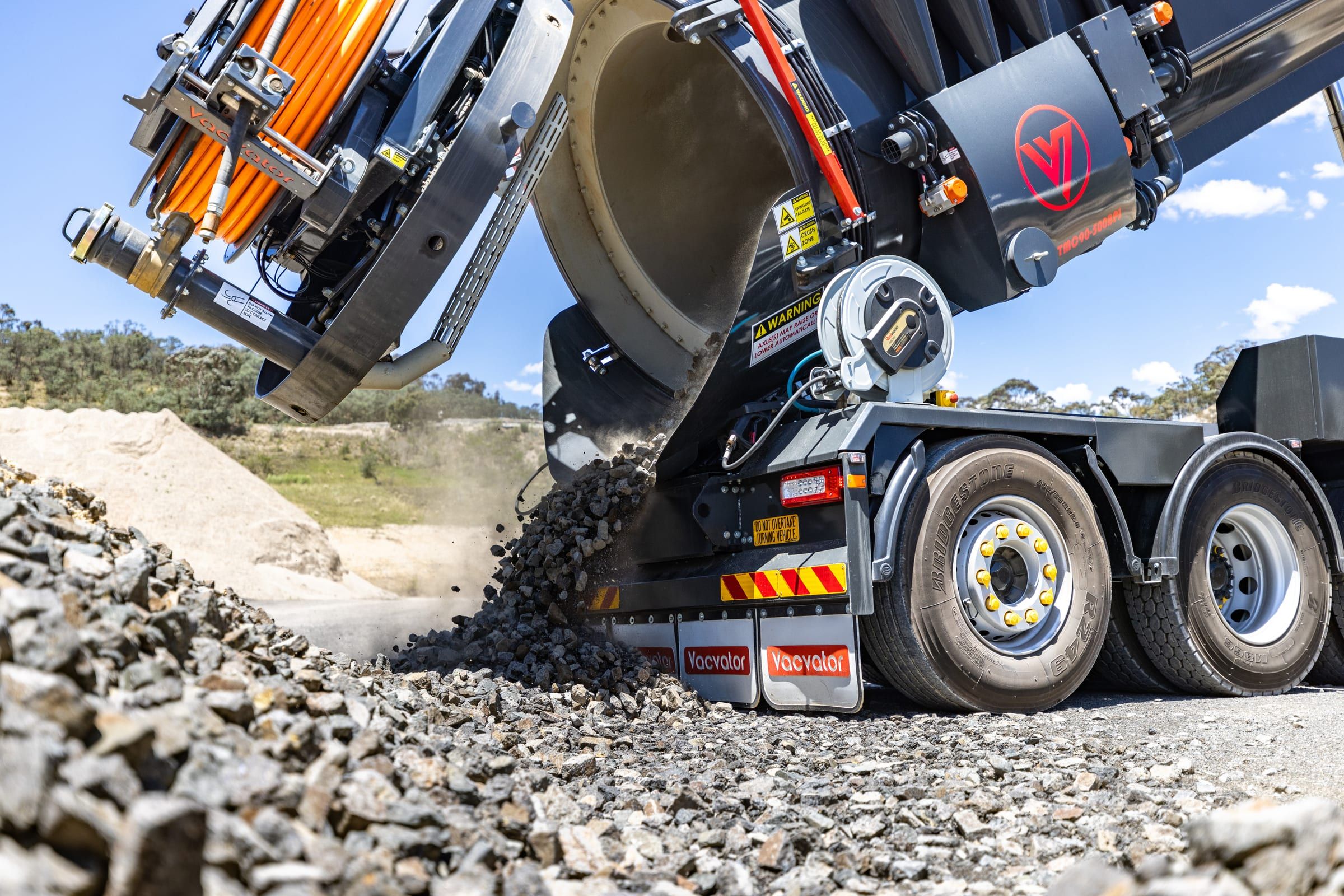 Low angle of gravel pouring from the tipped tank past the truck's rear wheels.